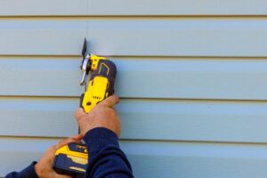 Damaged vinyl siding is removed using multi tool during reconstruction of house